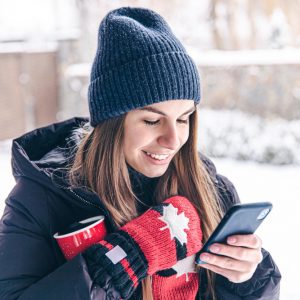 happy-young-woman-mittens-with-cup-looks-phone-screen (1)